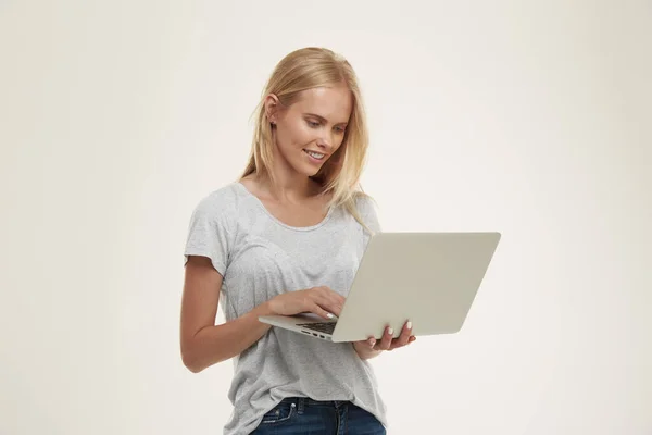 年轻的微笑的欧洲女孩拿着和使用笔记本电脑 漂亮的金发少女 蓝眼睛 穿着白色T恤和牛仔裤 被白色背景隔离 工作室拍摄 — 图库照片