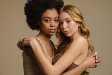 Bej arka planda duran iç çamaşırlı iki farklı genç kadın. Yakın plan.