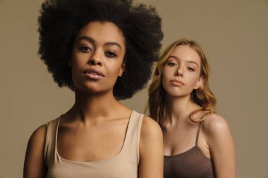 Bej arka planda duran iç çamaşırlı iki farklı genç kadın. Yakın plan.