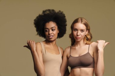 Bej arka planda duran iç çamaşırlı iki farklı genç kadın parmak kaldırıyor.
