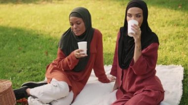 İki pozitif Müslüman kadın piknik battaniyesinde otururken içki içiyor.