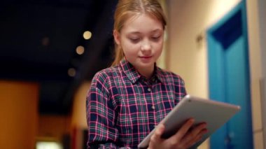 Kareli gömlek giyen, tabletle yazan konsantre bir kız öğrenci.