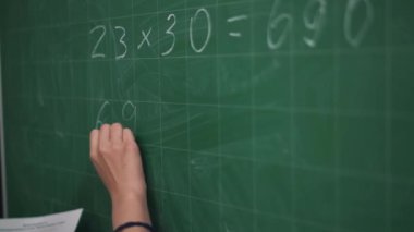 Asyalı kızın yakın plan görüntüsü tahtaya bir matematik örneği yazıyor.