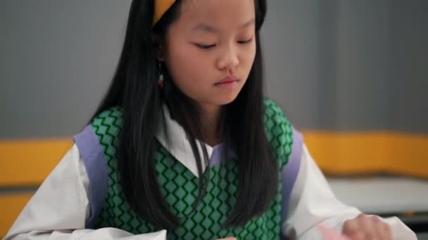 集中注意力的亚洲女孩在学校的练习本上写东西 — 图库视频影像