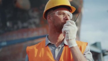 Üniformalı ciddi bir gemi yapımcısı dışarıda telsizle konuşuyor.