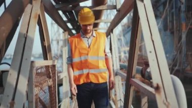 Üniformalı bir adam metal bir köprüden geçiyor kaskını çıkarıyor.