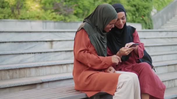 Twee Positieve Moslimvrouwen Kijken Naar Telefoon Trap Buiten — Stockvideo