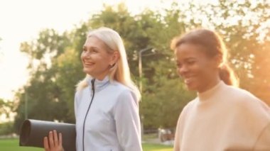 Çok uluslu gülümseyen olgun kadınlar dışarıda yogaya gidiyorlar.