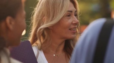 Sarışın, olgun bir kadın dışarıda arkadaşlarıyla konuşuyor.