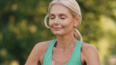 Olgun bir kadının açık havada meditasyon yaparken yakın plan görüntüsü.