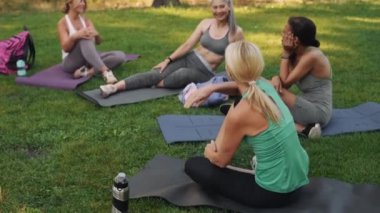 Çok uluslu gülümseyen olgun kadınlar dışarıda yoga minderinde konuşuyorlar.