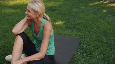 Dışarıda yoga minderinde gülümseyen olgun bir kadın.