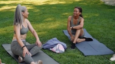 Parkta yoga minderinde konuşan çok uluslu olgun kadınlar.