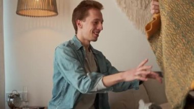 Gülümseyen adam odada yatakta otururken erkek arkadaşına süveter giydirir.