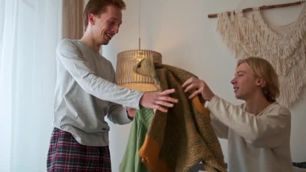 Przystojny Gej Para Próbuje Sweter Podczas Siedząc Łóżko Pokój — Wideo stockowe