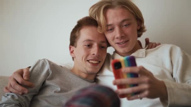 Skrattande Homosexuella Par Tittar Telefonen Och Pratar Sängen — Stockvideo