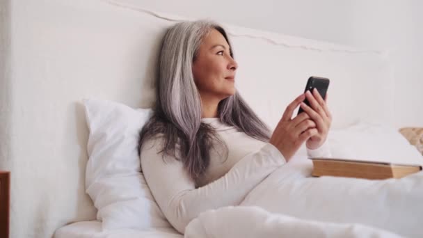 Pensativo Mujer Asiática Mirando Lado Teléfono Cama — Vídeos de Stock