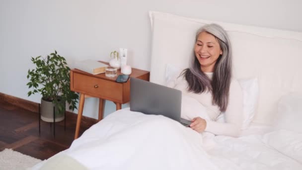 ベッドの上でラップトップでビデオ通話で話すアジアの女性 — ストック動画