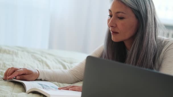 Skoncentrowany Azji Kobieta Czytanie Książki Patrząc Laptopa Podłodze — Wideo stockowe