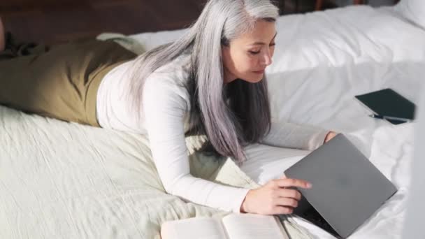 Smiling Asian Woman Typing Laptop While Lying Bed — Stock Video