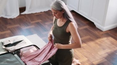 Yakışıklı Asyalı kadın evde bir bavulda eşyalarını topluyor.