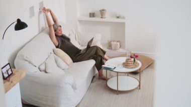 Evde dizüstü bilgisayara bakarken esneme hareketleri yapan pozitif Asyalı kadın.