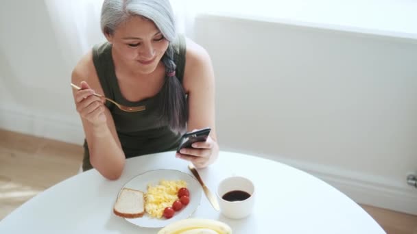 Asiática Sonriente Mujer Comiendo Desayuno Mirando Teléfono — Vídeo de stock