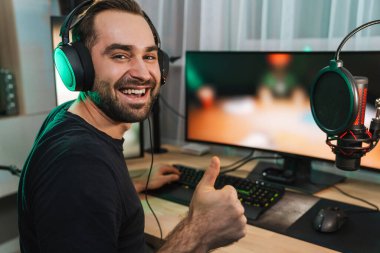 Mutlu genç oyuncu kulaklıkla bilgisayar başında oyuncularla sohbet ederek oyun yarışmasında zaferi kutluyor.