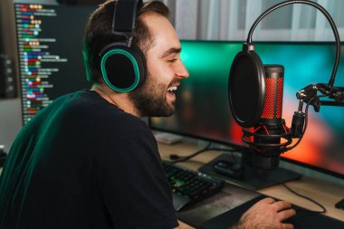 Bilgisayarda oynayan, oyuncularla konuşan, oyun yarışmasında konuşan, kulaklıklı mutlu genç oyuncu flaması.