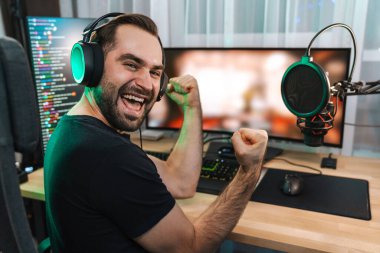 Mutlu genç oyuncu kulaklıkla bilgisayar başında oyuncularla sohbet ederek oyun yarışmasında zaferi kutluyor.