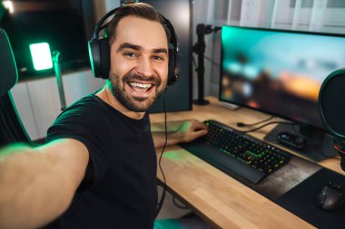 Mutlu genç adam evde bilgisayar başında video oyunu oynarken fotoğraf çekiyor ve başarıyı kutluyor.