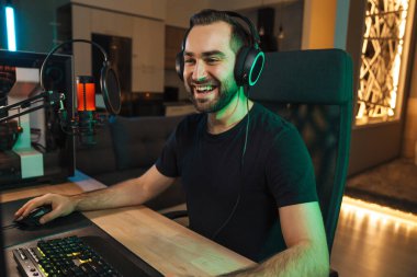 Bilgisayarda oynayan, oyuncularla konuşan, oyun yarışmasında konuşan, kulaklıklı mutlu genç oyuncu flaması.