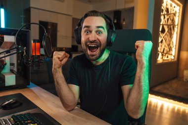 Mutlu genç oyuncu kulaklıkla bilgisayar başında oyuncularla sohbet ederek oyun yarışmasında zaferi kutluyor.