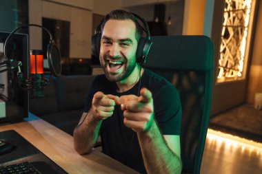Mutlu genç oyuncu kulaklıkla bilgisayar başında oyuncularla sohbet ederek oyun yarışmasında zaferi kutluyor.
