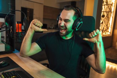 Mutlu genç oyuncu kulaklıkla bilgisayar başında oyuncularla sohbet ederek oyun yarışmasında zaferi kutluyor.