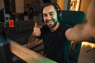 Mutlu genç adam evde bilgisayar başında video oyunu oynarken fotoğraf çekiyor ve başarıyı kutluyor.