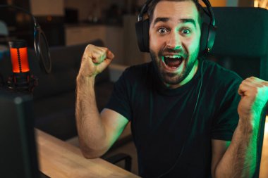 Mutlu genç oyuncu kulaklıkla bilgisayar başında oyuncularla sohbet ederek oyun yarışmasında zaferi kutluyor.