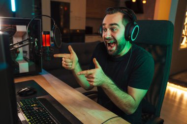Mutlu genç oyuncu kulaklıkla bilgisayar başında oyuncularla sohbet ederek oyun yarışmasında zaferi kutluyor.