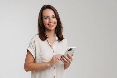Beyaz arka planda izole edilmiş cep telefonu kullanırken gülümseyen genç esmer kadın.