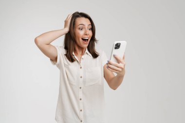 Beyaz arka plan üzerinde izole cep telefonu kullanan genç bir kadın başını tutuyor.