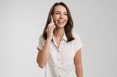 Genç Avrupalı kadın, beyaz arka planda izole bir şekilde cep telefonuyla konuşurken gülüyor