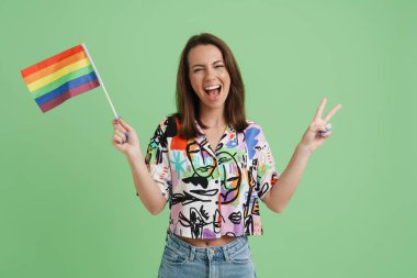 Genç Avrupalı kadın yeşil arka planda izole edilmiş gökkuşağı bayrağıyla poz verirken el kol hareketi yapıyor