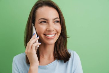 Genç esmer kadın yeşil arka plandan izole edilmiş cep telefonuyla konuşurken gülüyor.