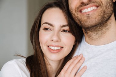 Evde kucaklaşırken gülümseyen çok kültürlü genç bir çift.