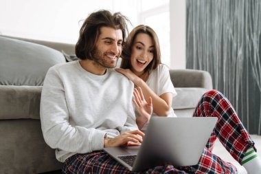 Genç, çok ırklı bir çift evde otururken diz üstü bilgisayar kullanıyor.