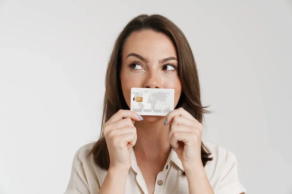 年轻的黑发女子一边摆姿势一边看一边拿着白色背景的信用卡 — 图库照片