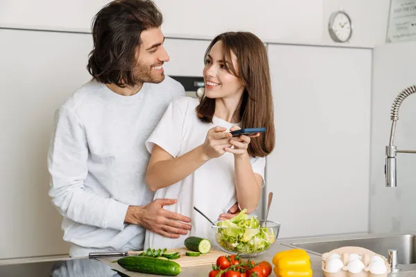 Jovem Casal Multirracial Usando Celular Abraços Enquanto Cozinham Juntos Casa — Fotografia de Stock
