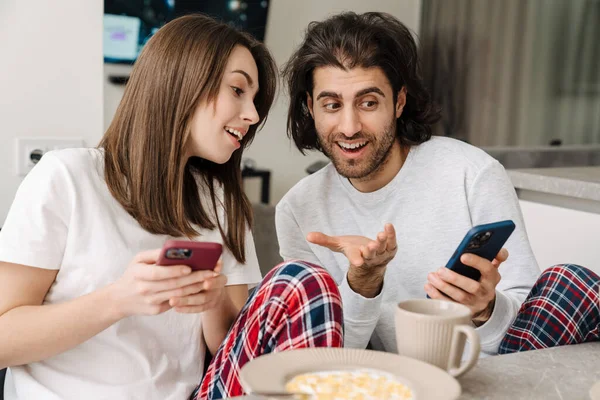 Joven Pareja Multirracial Usando Teléfonos Celulares Mientras Desayunan Juntos Casa —  Fotos de Stock