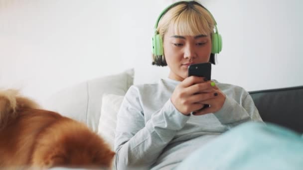 Alegre Mujer Asiática Mirando Teléfono Acariciando Perro Cama Casa — Vídeo de stock