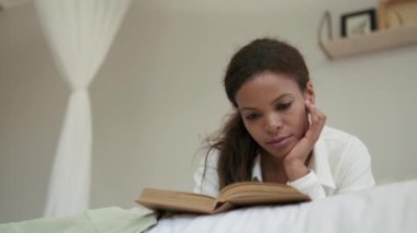Düşünceli Afrikalı kadın yatakta kitap okuyor.